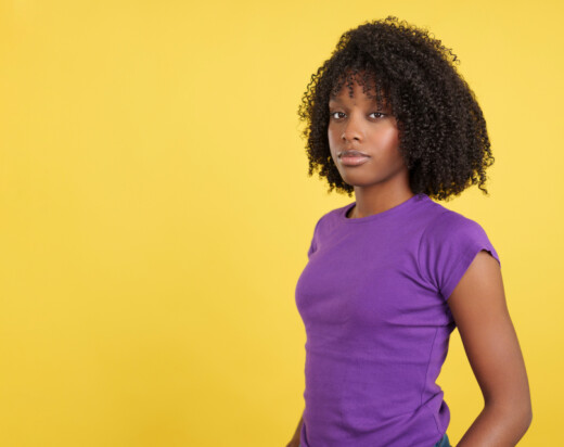 Serious woman with afro hair looking at camera in studio with yellow background